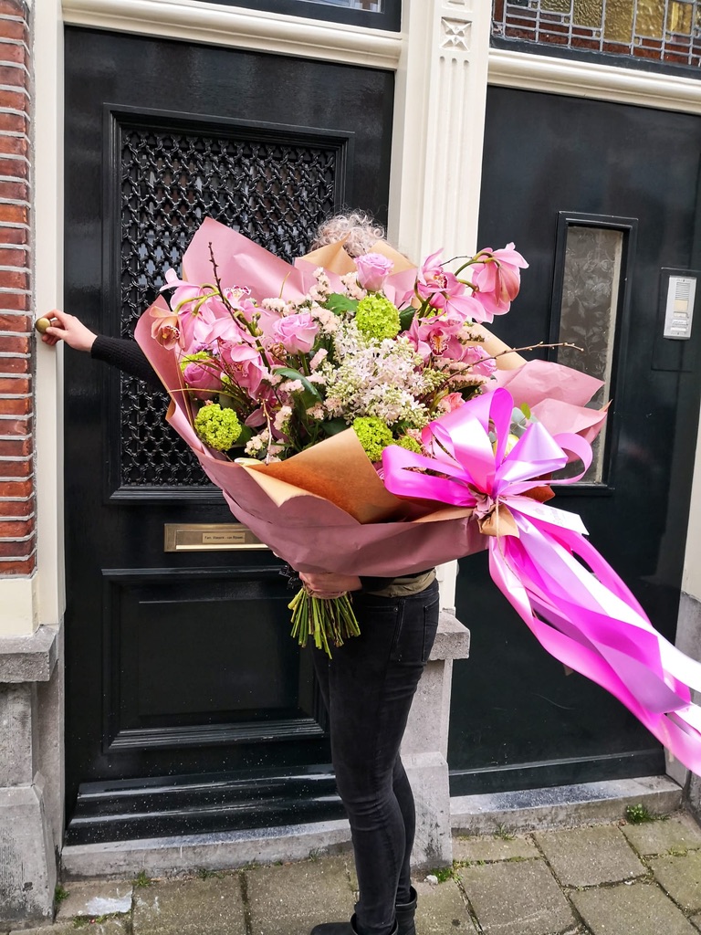 een medewerker van regina boemisten den haag die bloemen thuis bezorgen met een grote roze lind hieraan